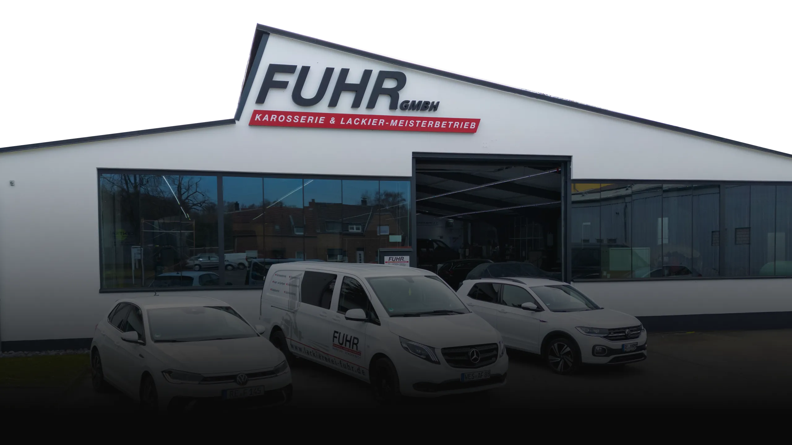 Außenansicht der Fuhr GmbH Karosserie & Lackier-Meisterbetrieb mit weißen Firmenfahrzeugen vor dem Gebäude.