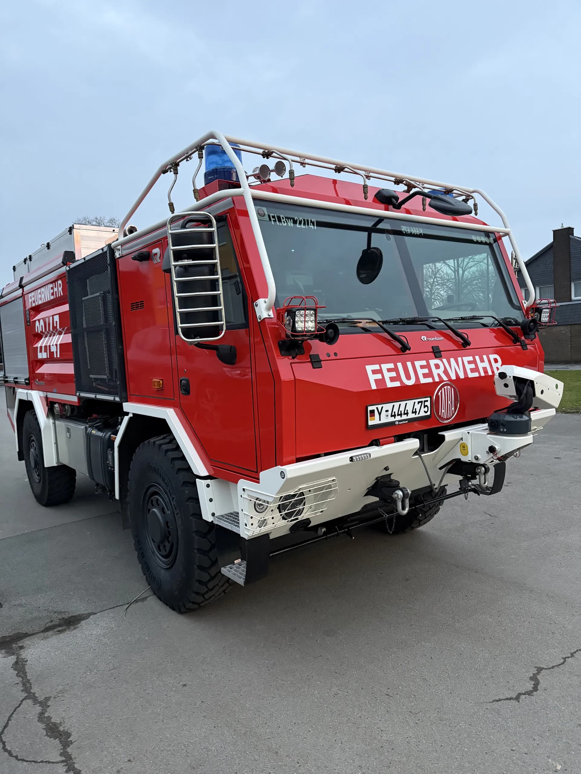Rotes Feuerwehrfahrzeug mit Blaulicht, Überrollkäfig und weißem Schriftzug Feuerwehr auf der Front.